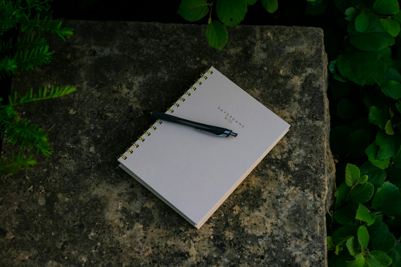 Spiral notebook and pen resting on a mossy stone garden wall