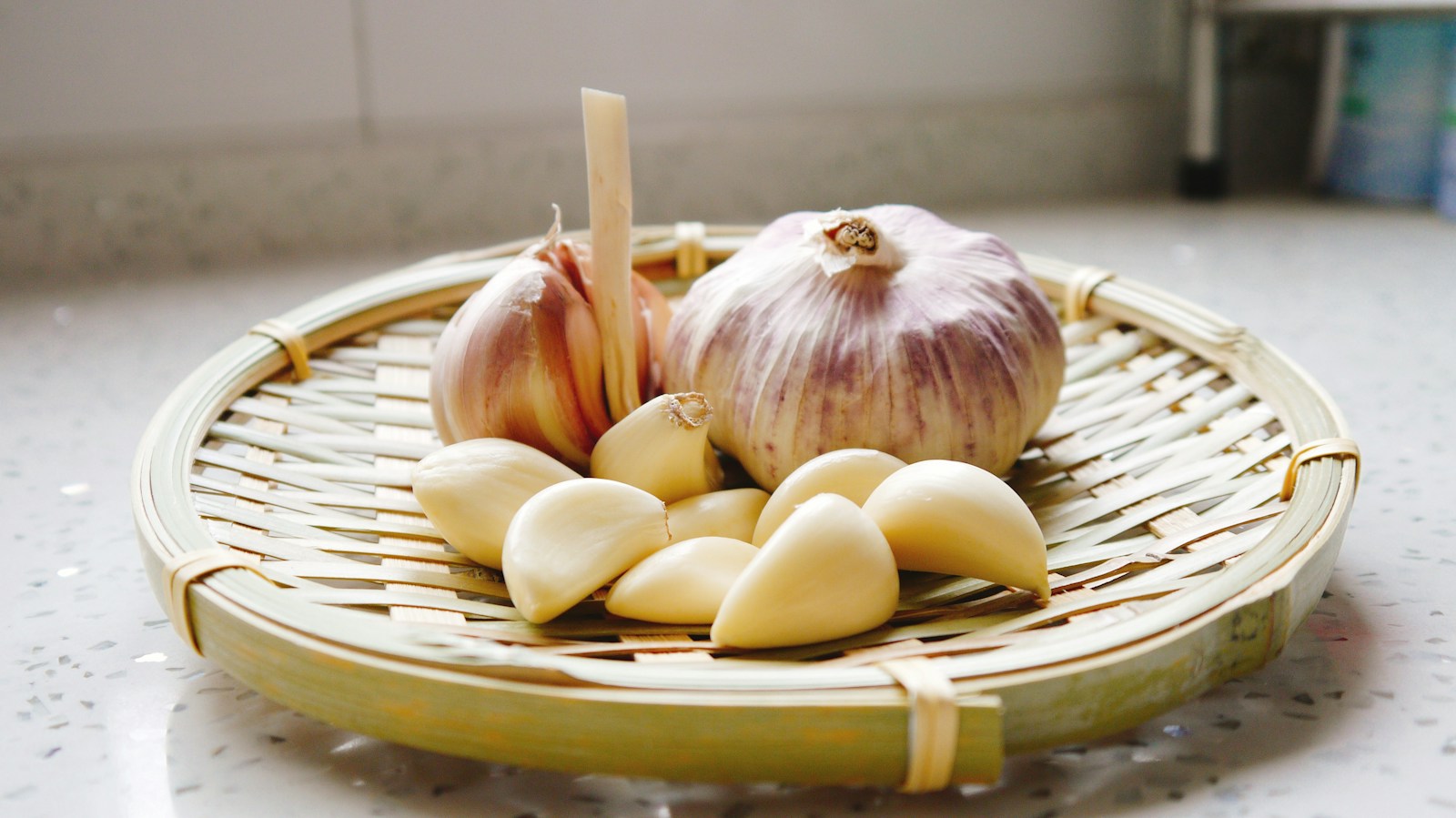 Purple-skinned garlic bulbs and peeled cloves on a bamboo tray
