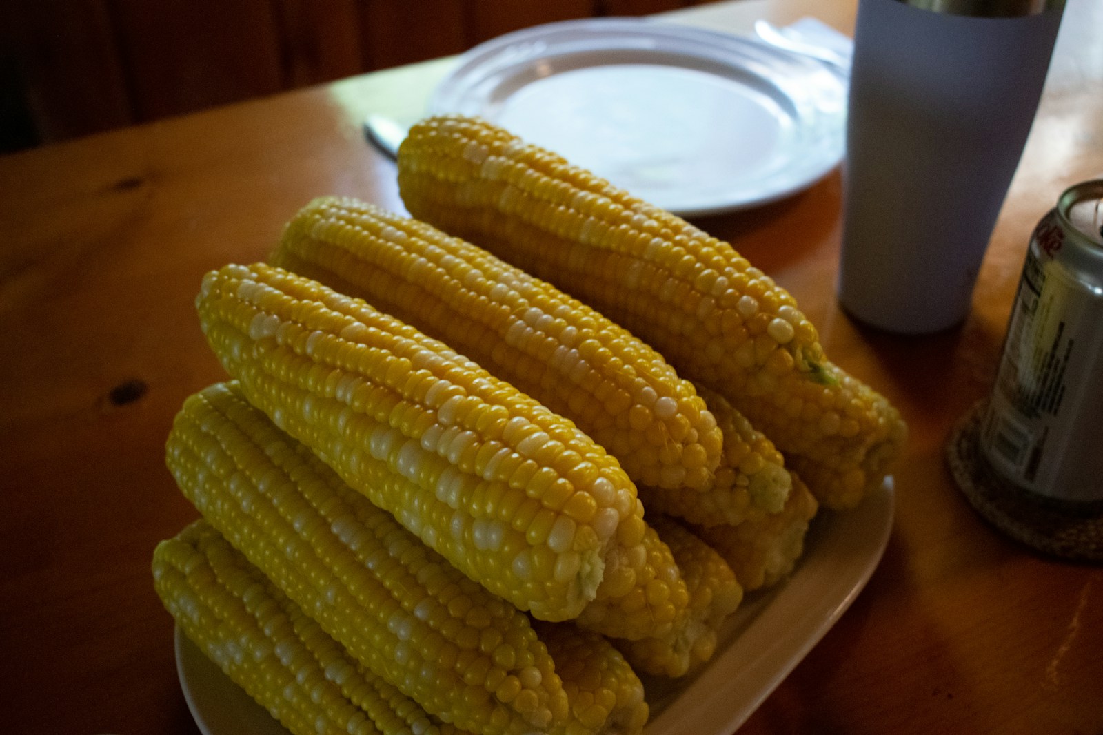 Husked yellow and white sweet corn cobs piled on a plate on a wooden table