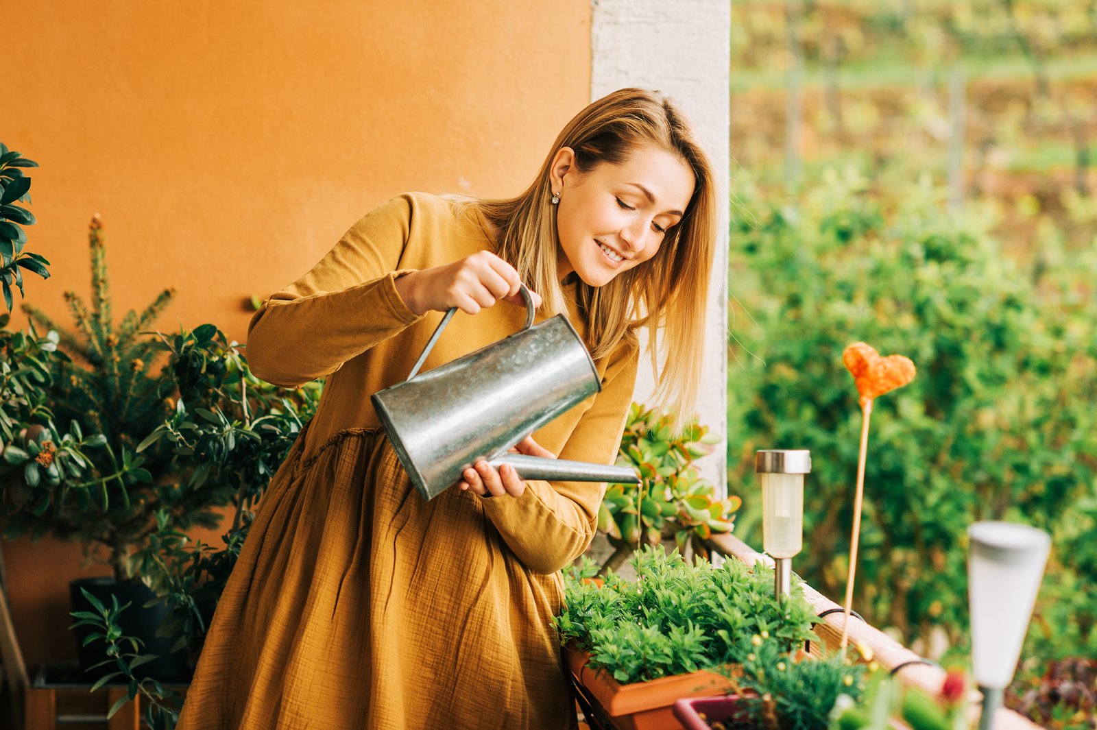 Woman watering container plants on a balcony with a metal watering can