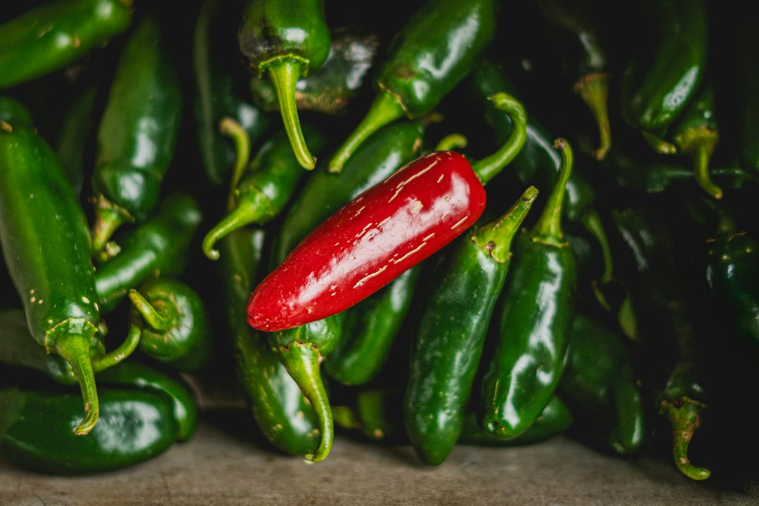 Pile of green jalapeño peppers with a single ripe red pod among them