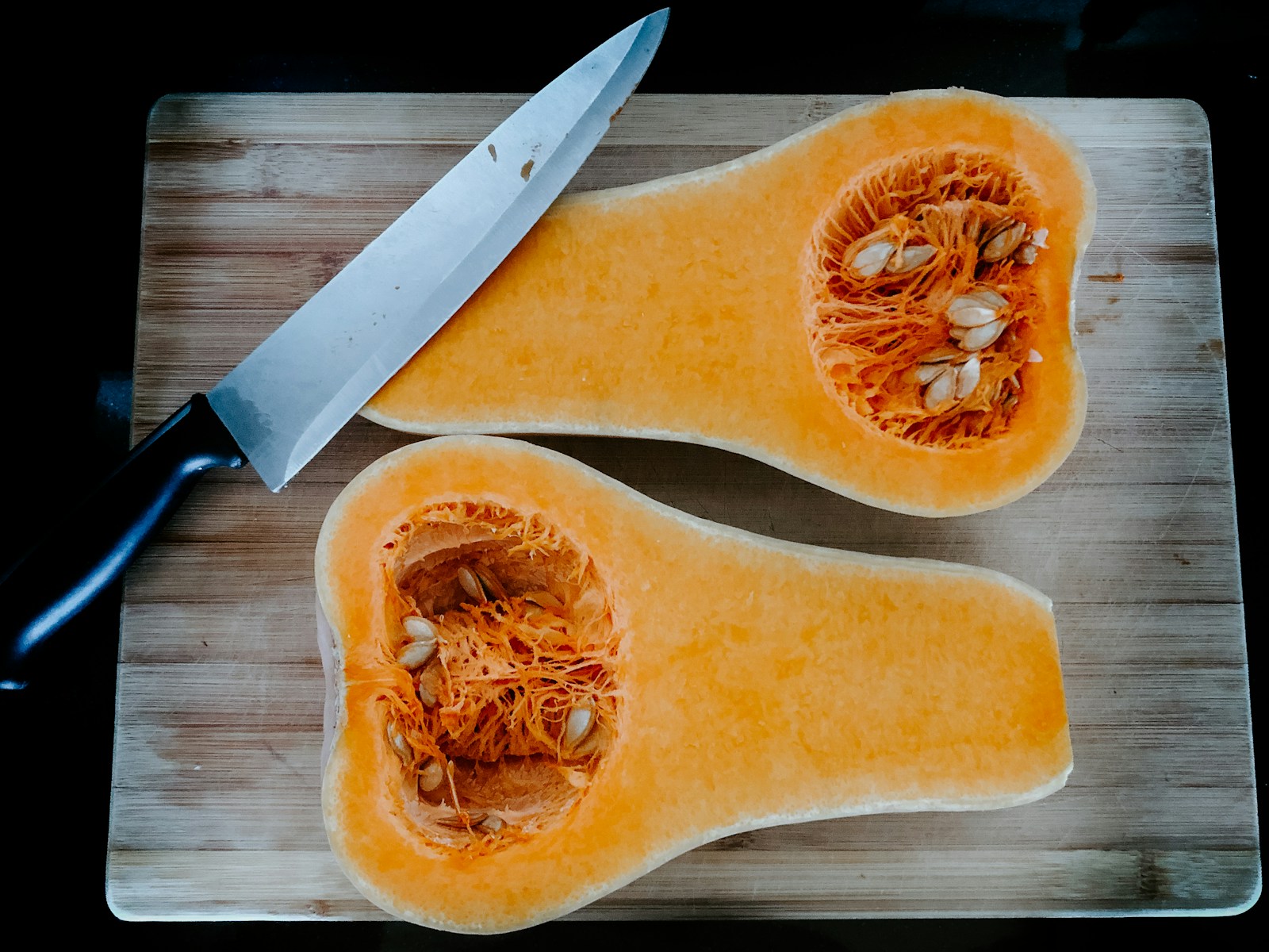 A butternut squash cut in half on a board, showing orange flesh and seeds