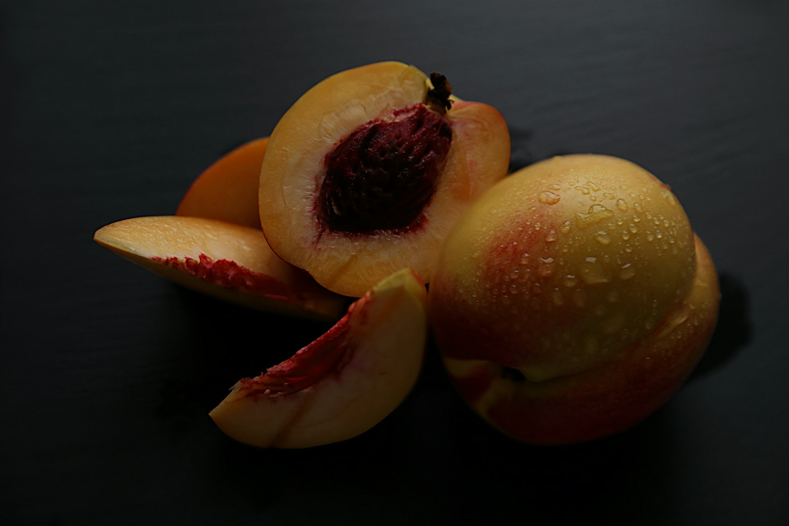 Smooth-skinned nectarines, whole and sliced to show the stone, on slate