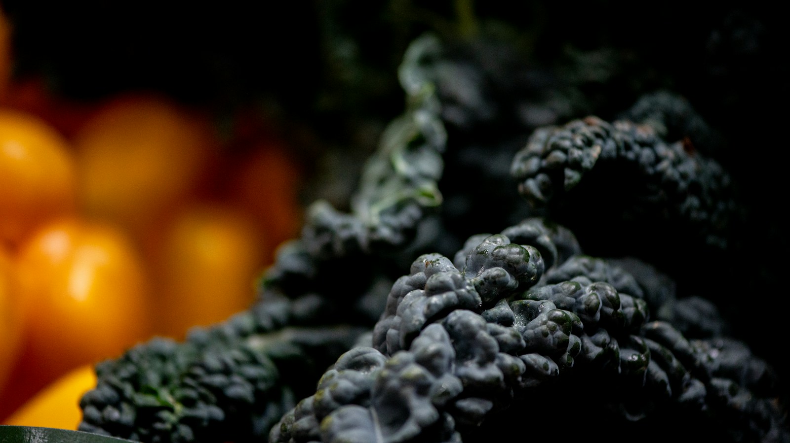 Dark, heavily blistered lacinato kale leaves beside blurred orange peppers