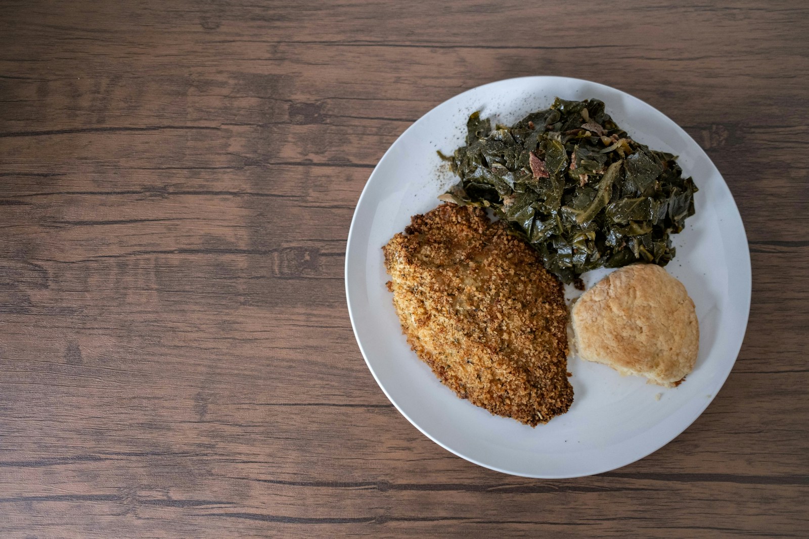 A plate of braised collard greens with breaded fish and a biscuit