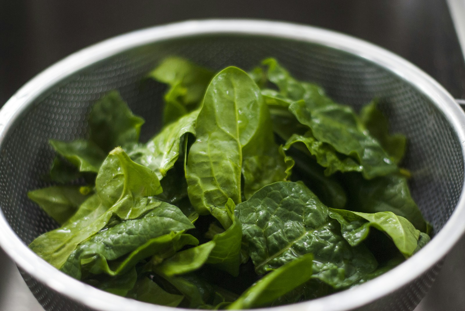 Washed spinach leaves draining in a stainless steel colander