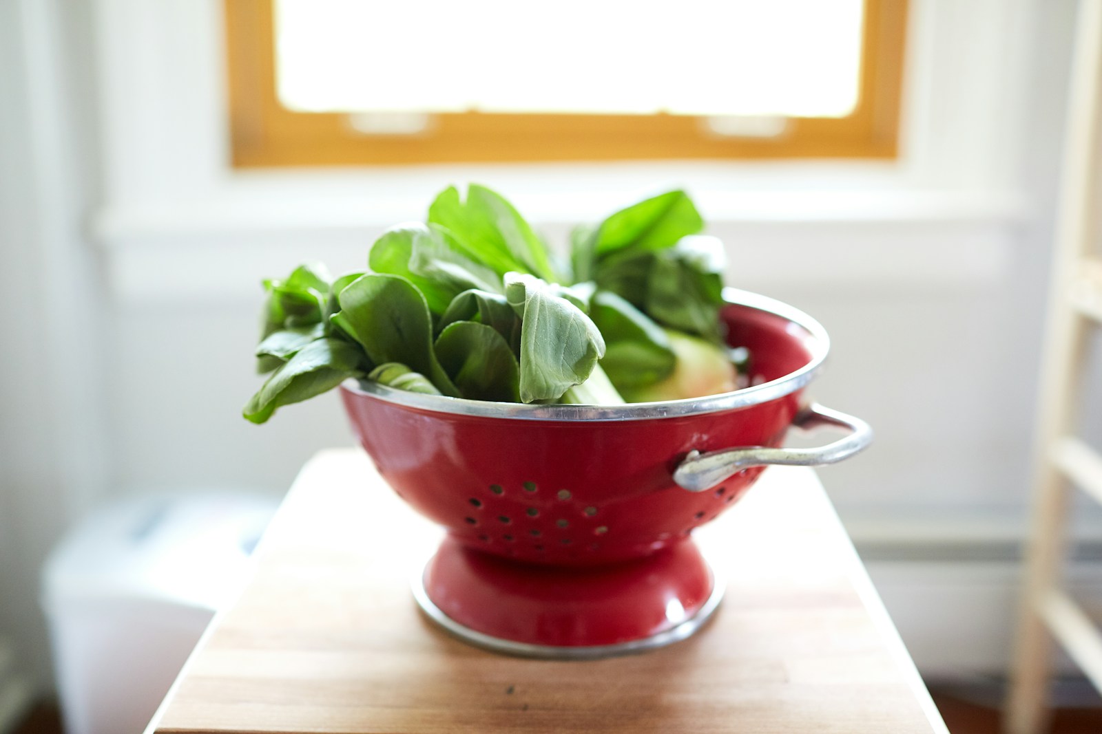 Freshly harvested bok choy heads in a red colander on a wooden table