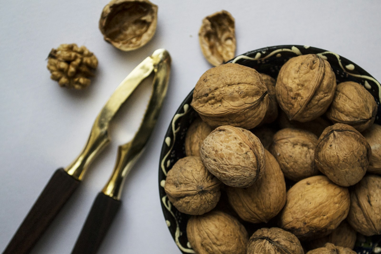 Bowl of thin-shelled English walnuts beside a brass nutcracker, for comparison