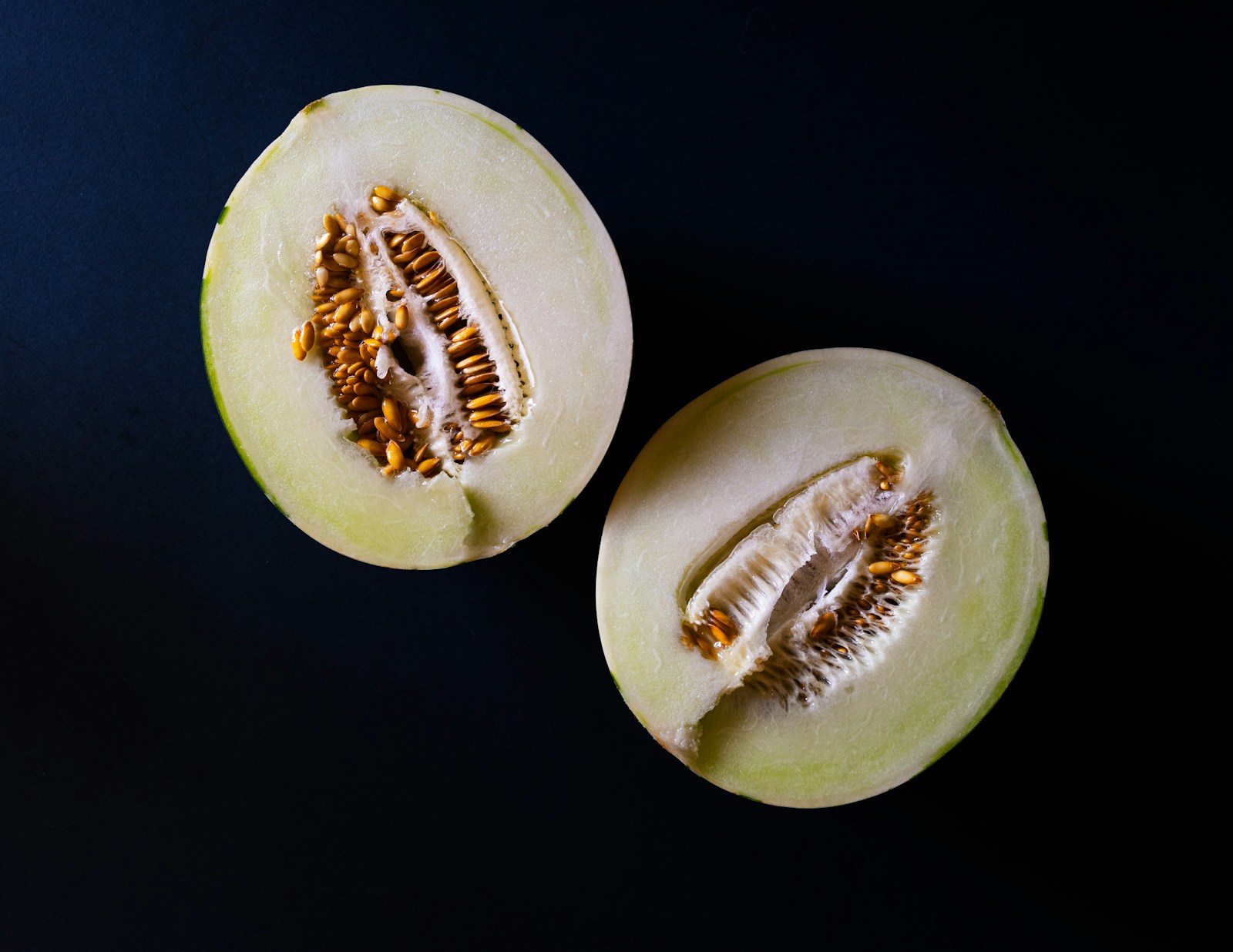 Two honeydew melon halves seen from above, seed cavities exposed