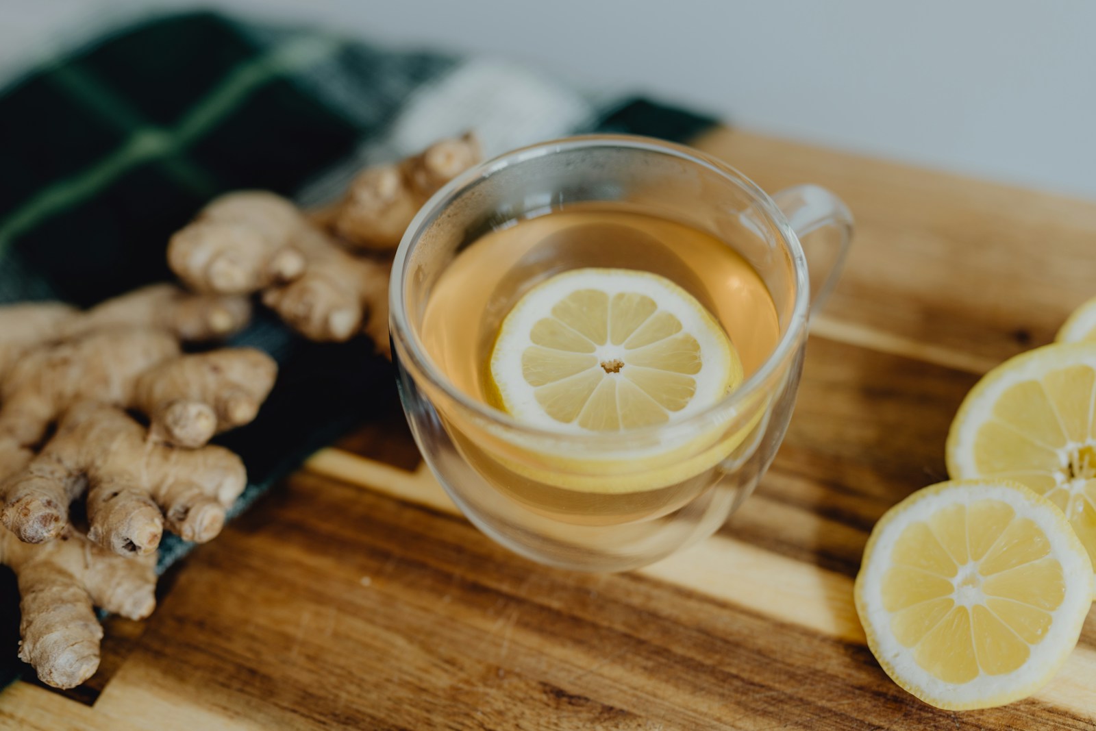 Glass cup of ginger tea with lemon slice beside fresh ginger rhizomes
