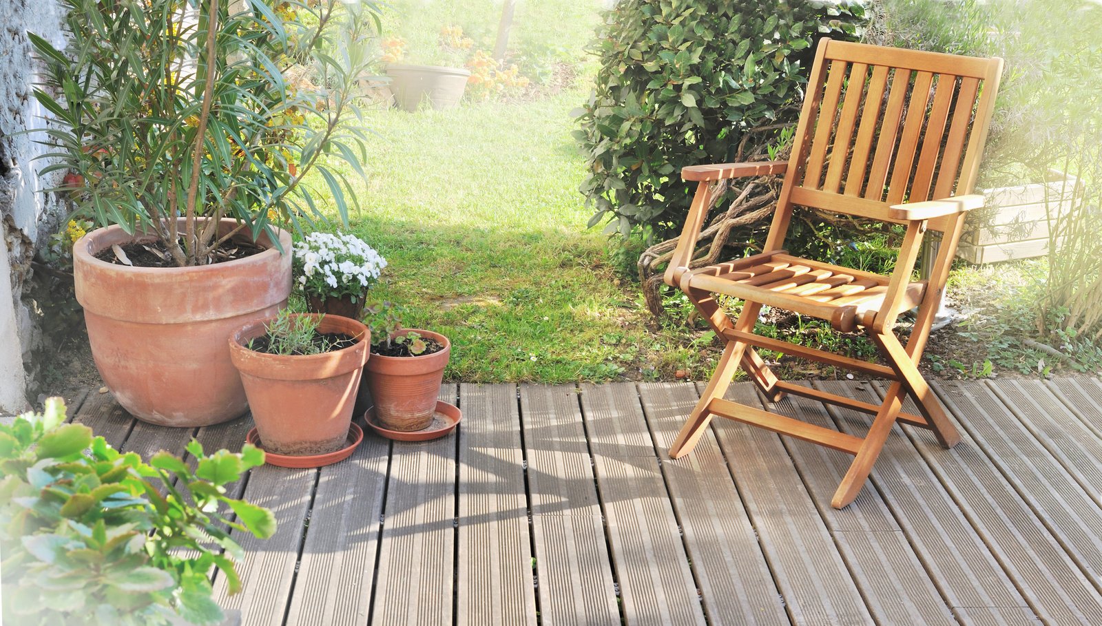 Terracotta pots standing in shade on a wooden deck beside a garden chair