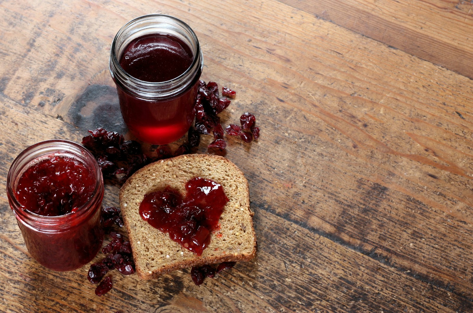 Two jars of dark red jelly and jam beside jam-spread bread