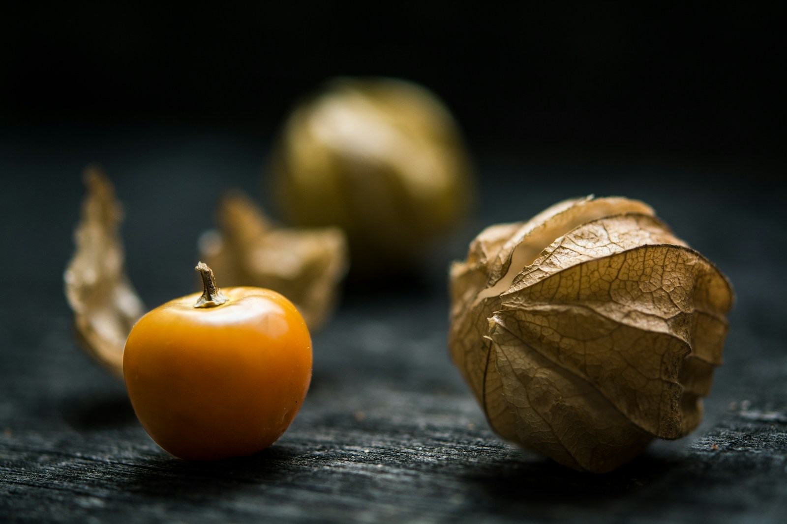 Husked orange cape gooseberry beside a dry, papery husk on dark wood