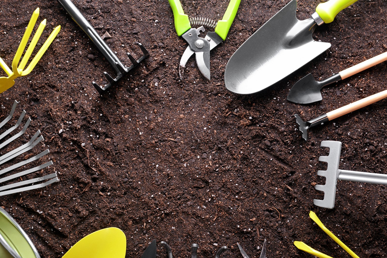 Hand rakes, trowel, pruners and other garden tools laid out on bare soil