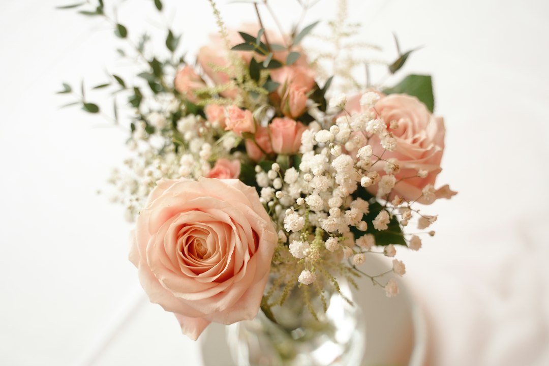 A glass vase of freshly cut peach and pink roses arranged with baby's breath and greenery