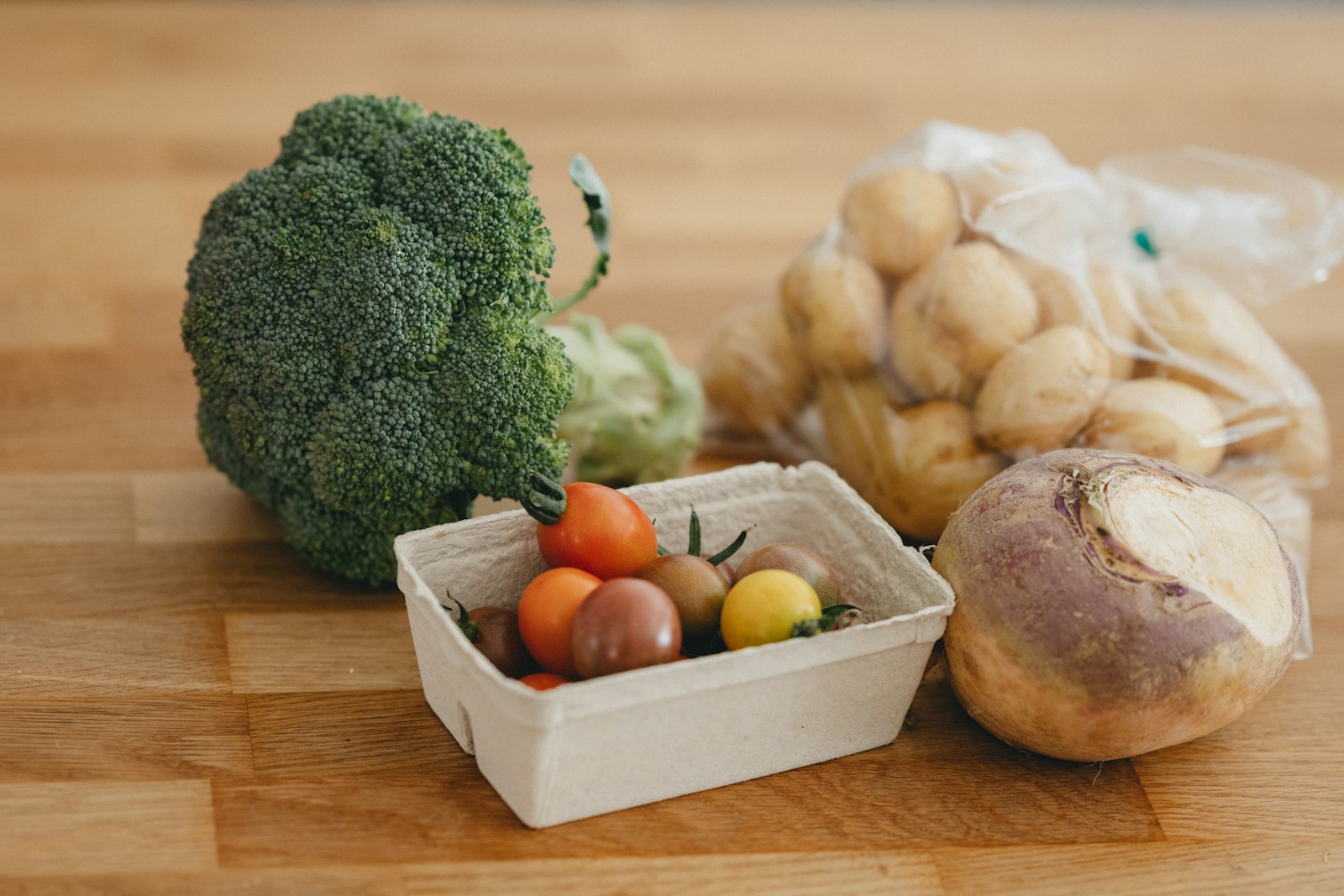 A single rutabaga root beside broccoli, cherry tomatoes and a bag of potatoes