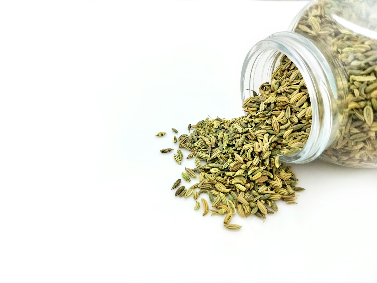 Dried fennel seeds spilling from a glass jar onto a white surface