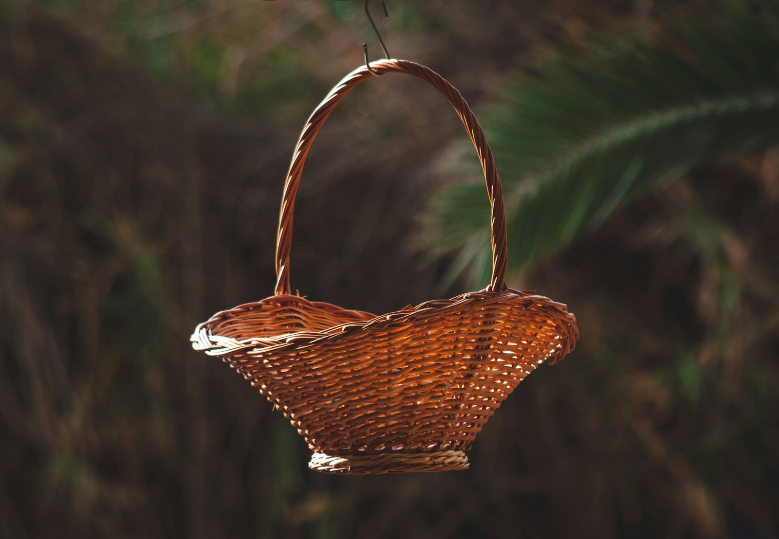 Empty woven wicker basket with a handle, hanging outdoors