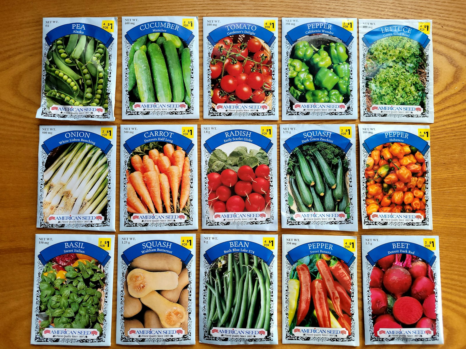 Fifteen vegetable and herb seed packets laid out in rows on a table