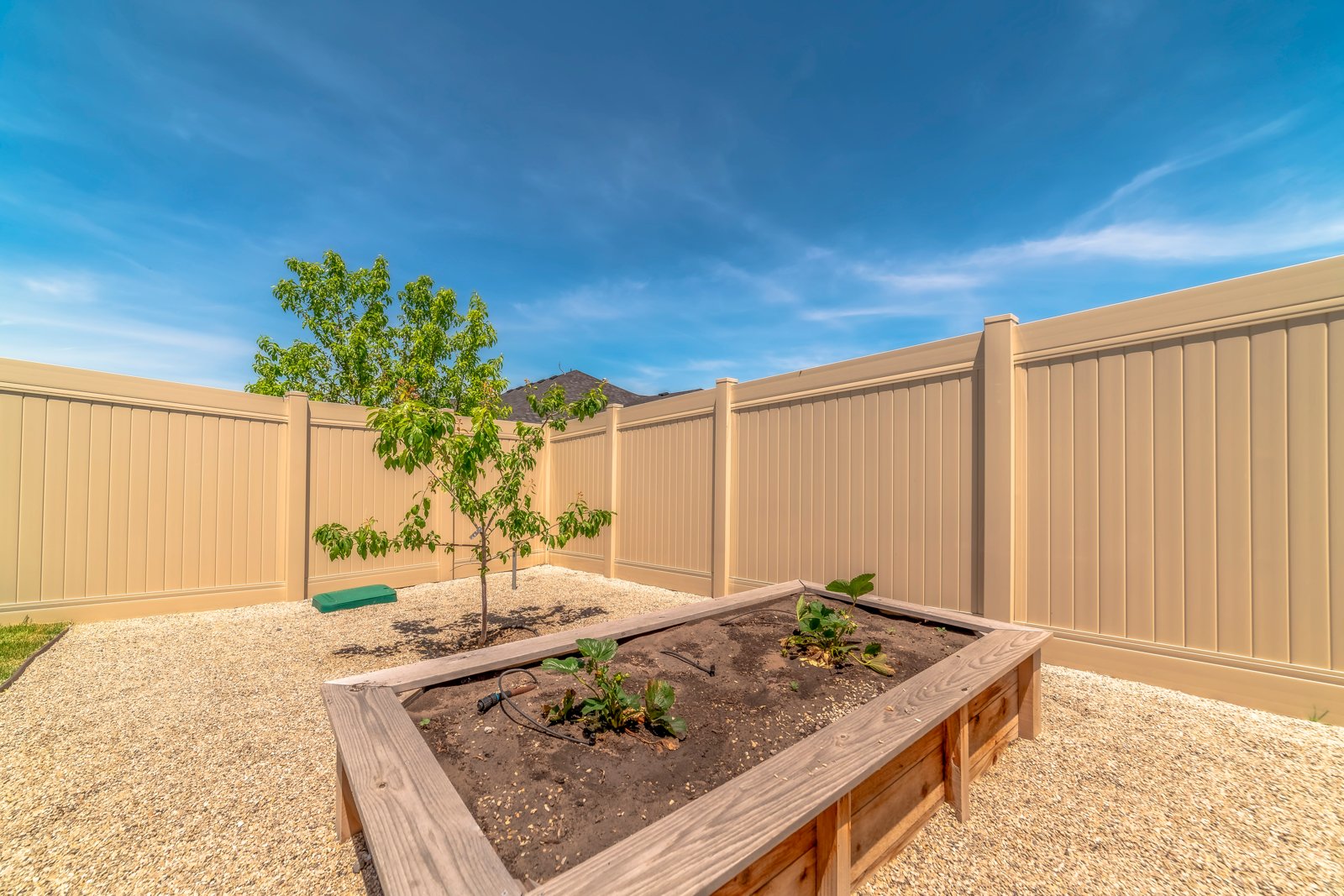 A wooden raised bed of bare soil in a sunny backyard