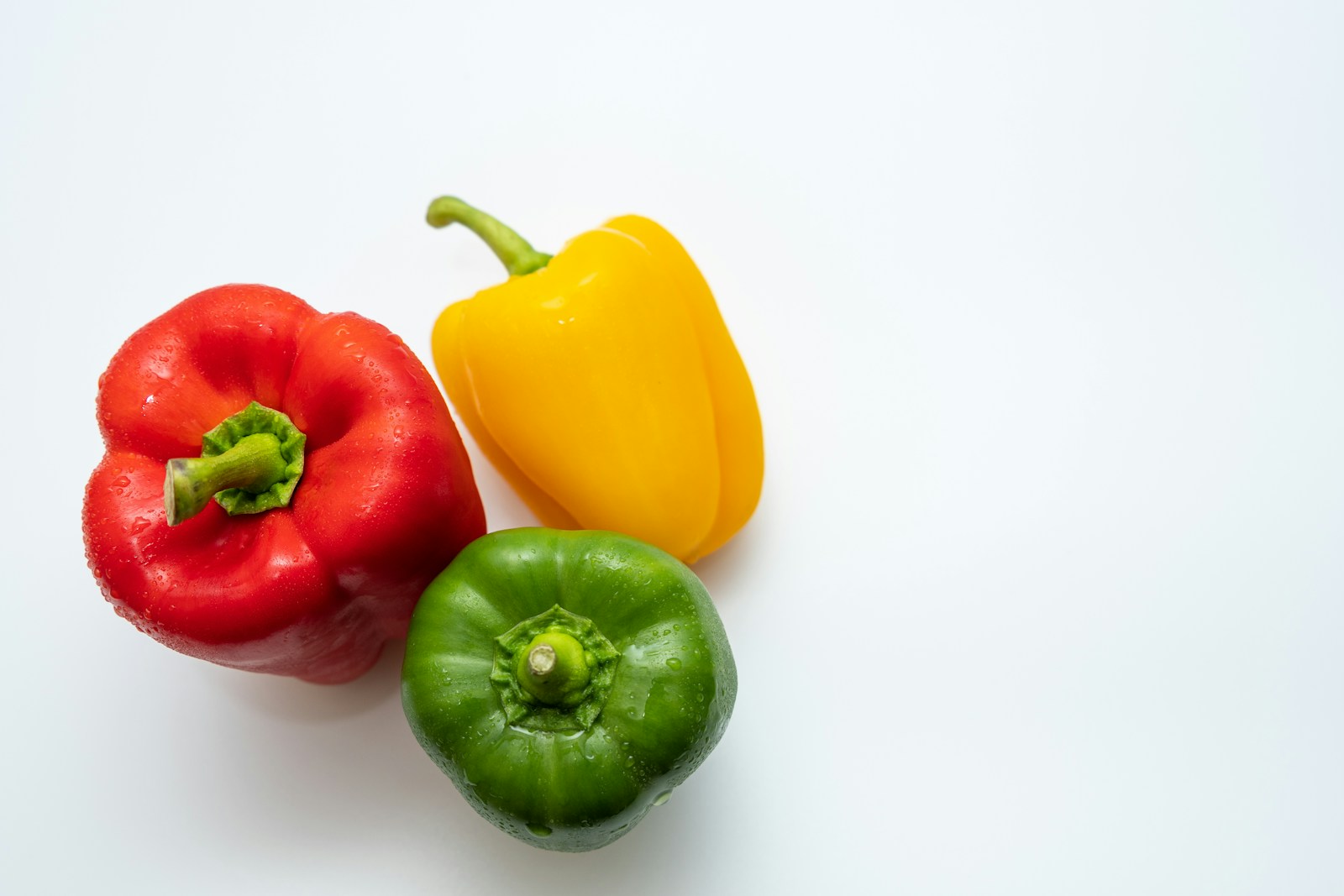 Red, yellow and green bell peppers side by side on white