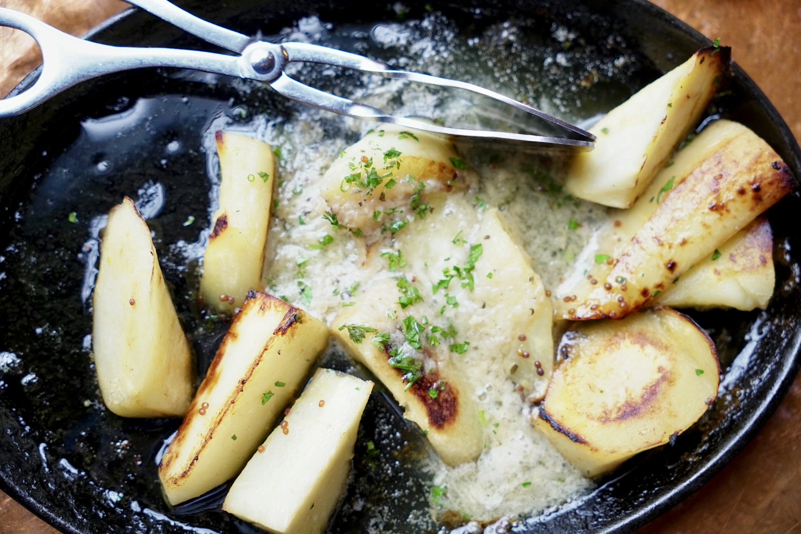 Roasted parsnip wedges with herbs and mustard seeds in a cast-iron dish