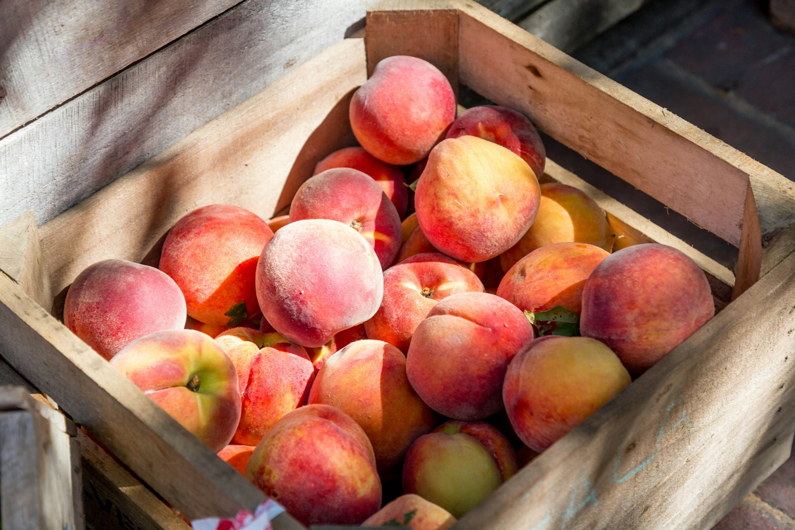 Wooden crate filled with freshly picked ripe peaches in sunlight