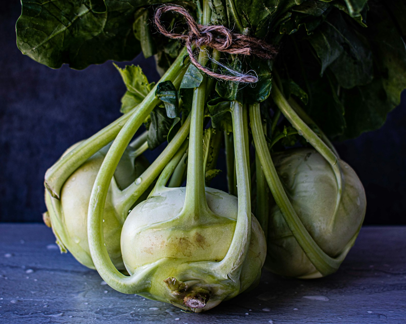 Three harvested green kohlrabi bulbs tied in a bunch by their leaf stalks