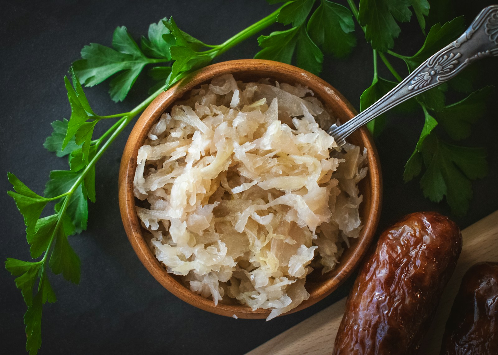 Wooden bowl of sauerkraut with a spoon, parsley and sausages