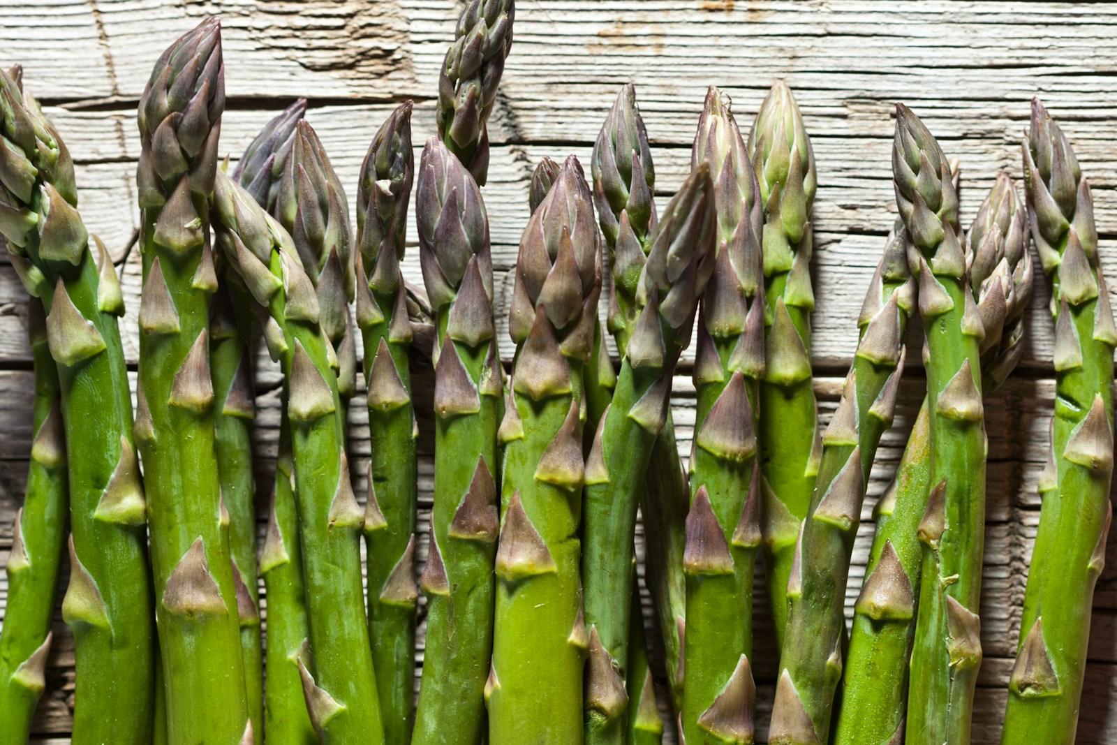 Row of thick green asparagus spears with purple-tinged tips on wood