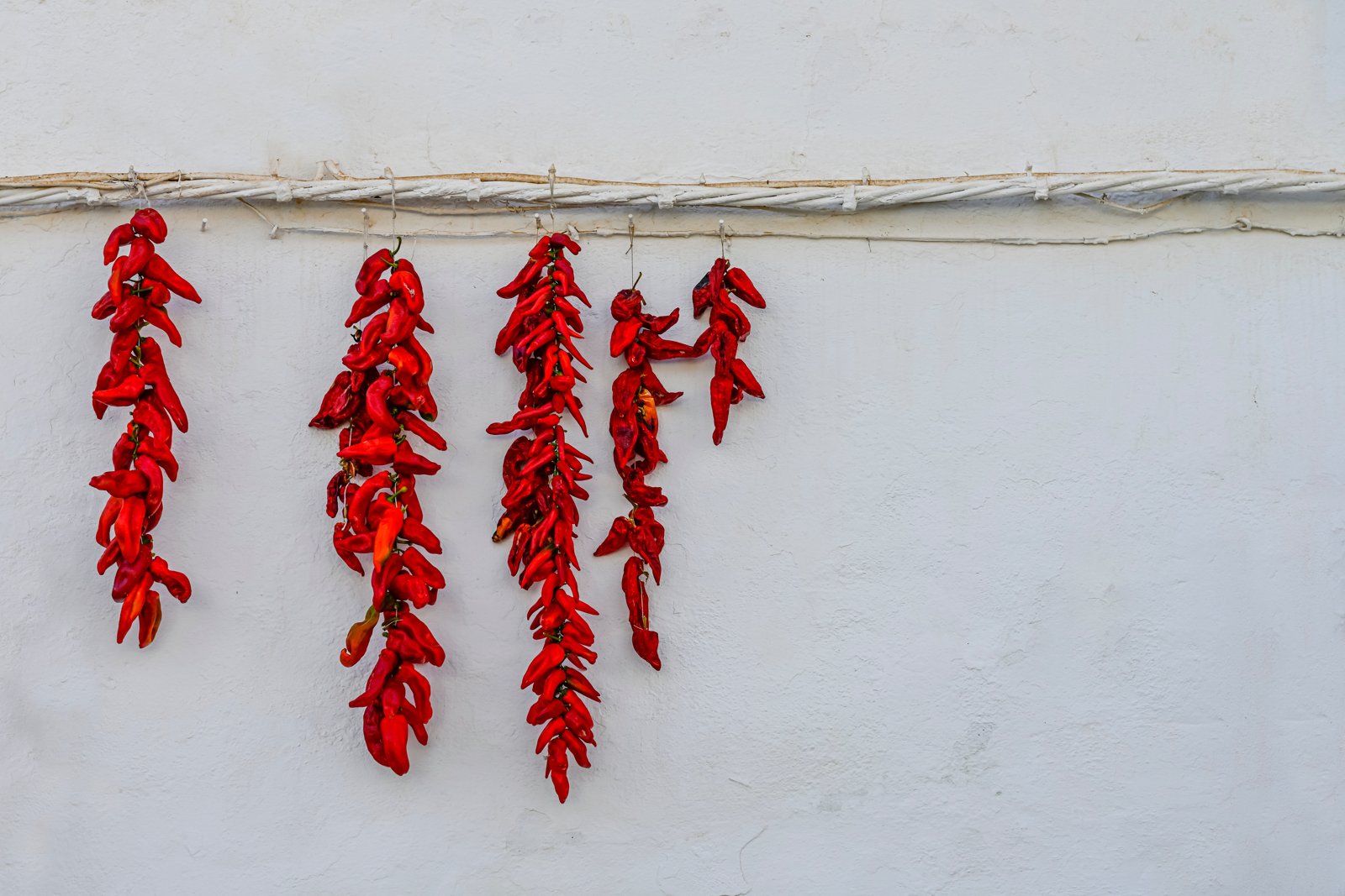 Strings of red chili peppers hanging to dry against a white wall