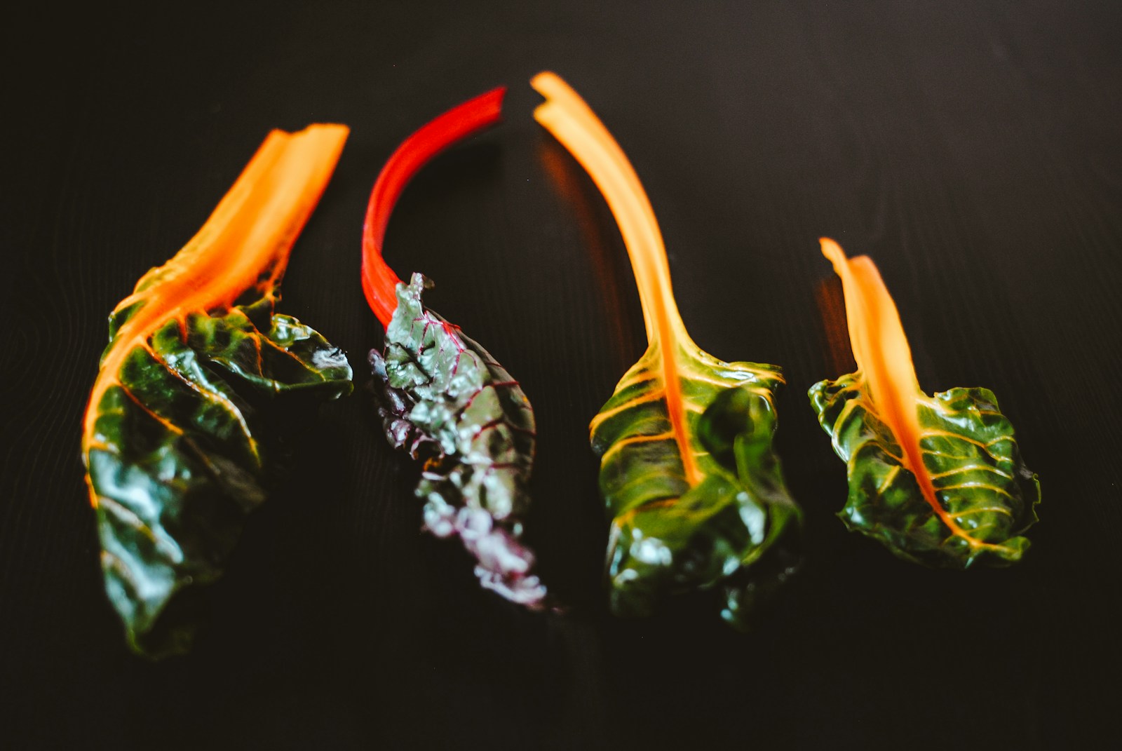 Four picked chard leaves with orange and red stems on a dark table