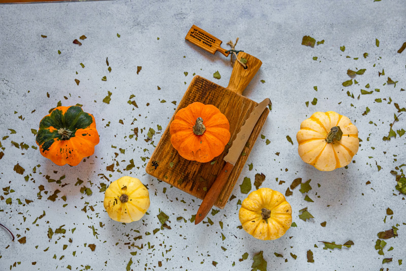 Palm-sized orange, yellow and striped miniature pumpkins around a small cutting board