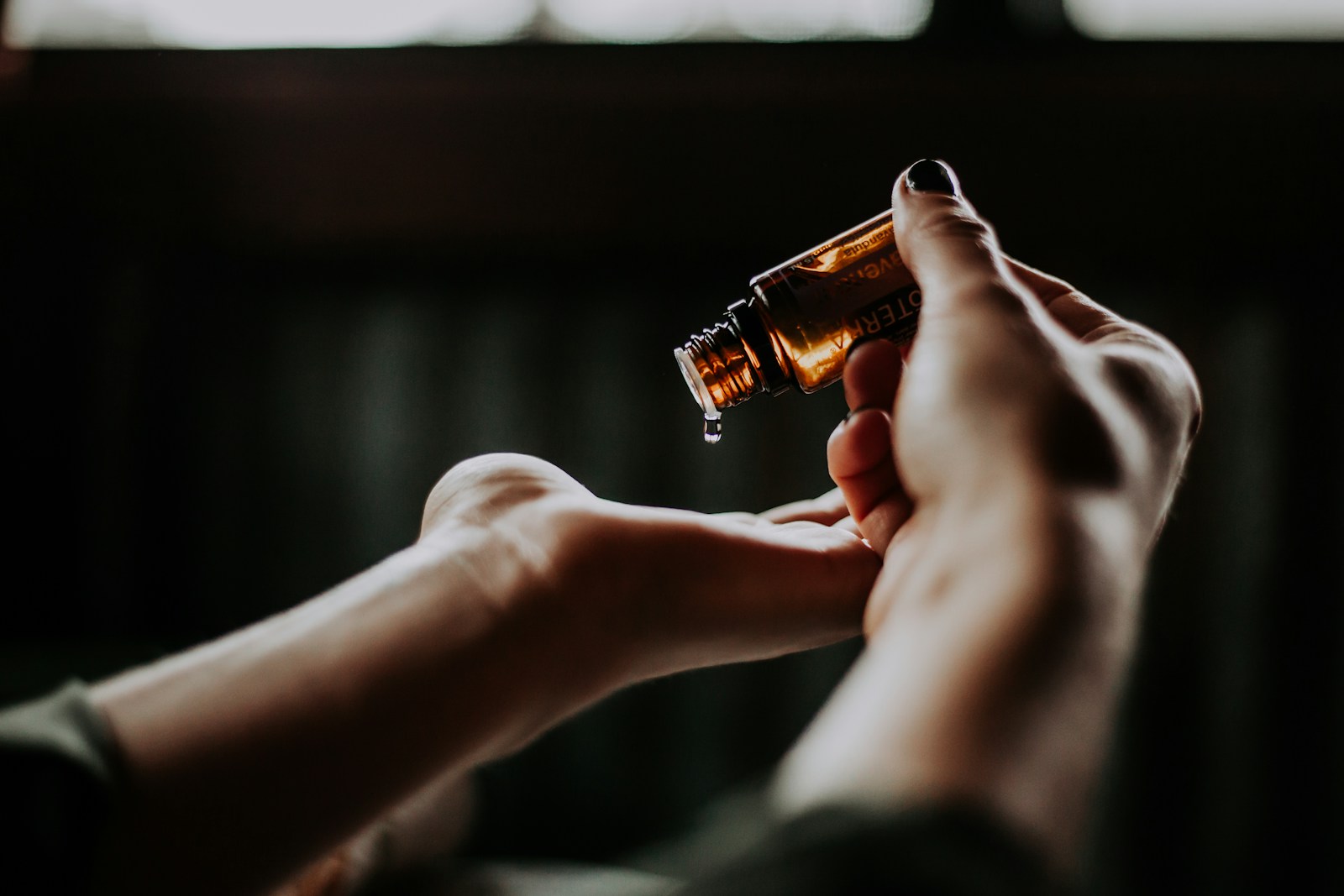 A hand tipping drops of oil from a small amber dropper bottle