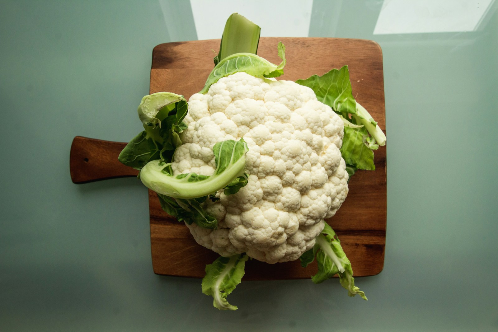 A whole white cauliflower head with wrapper leaves on a wooden board