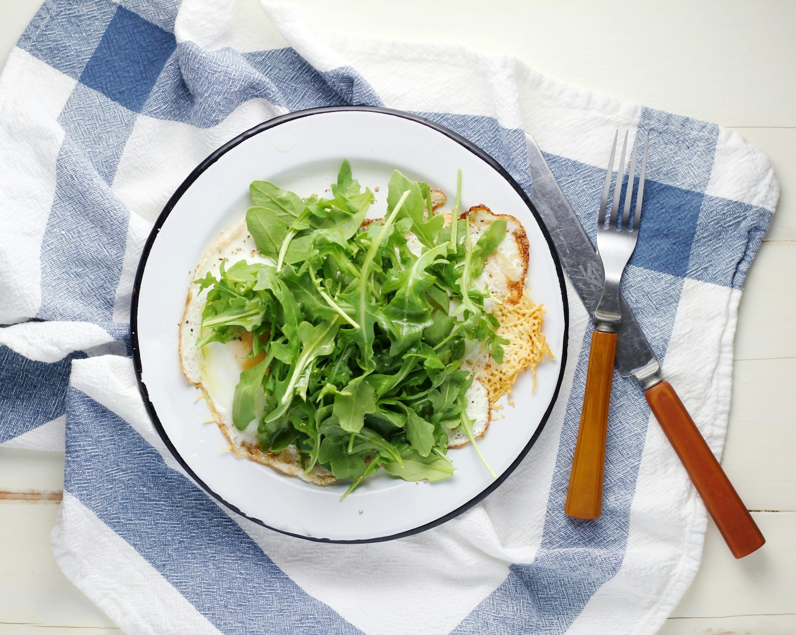 Fresh-picked arugula leaves piled on a fried egg on a white plate