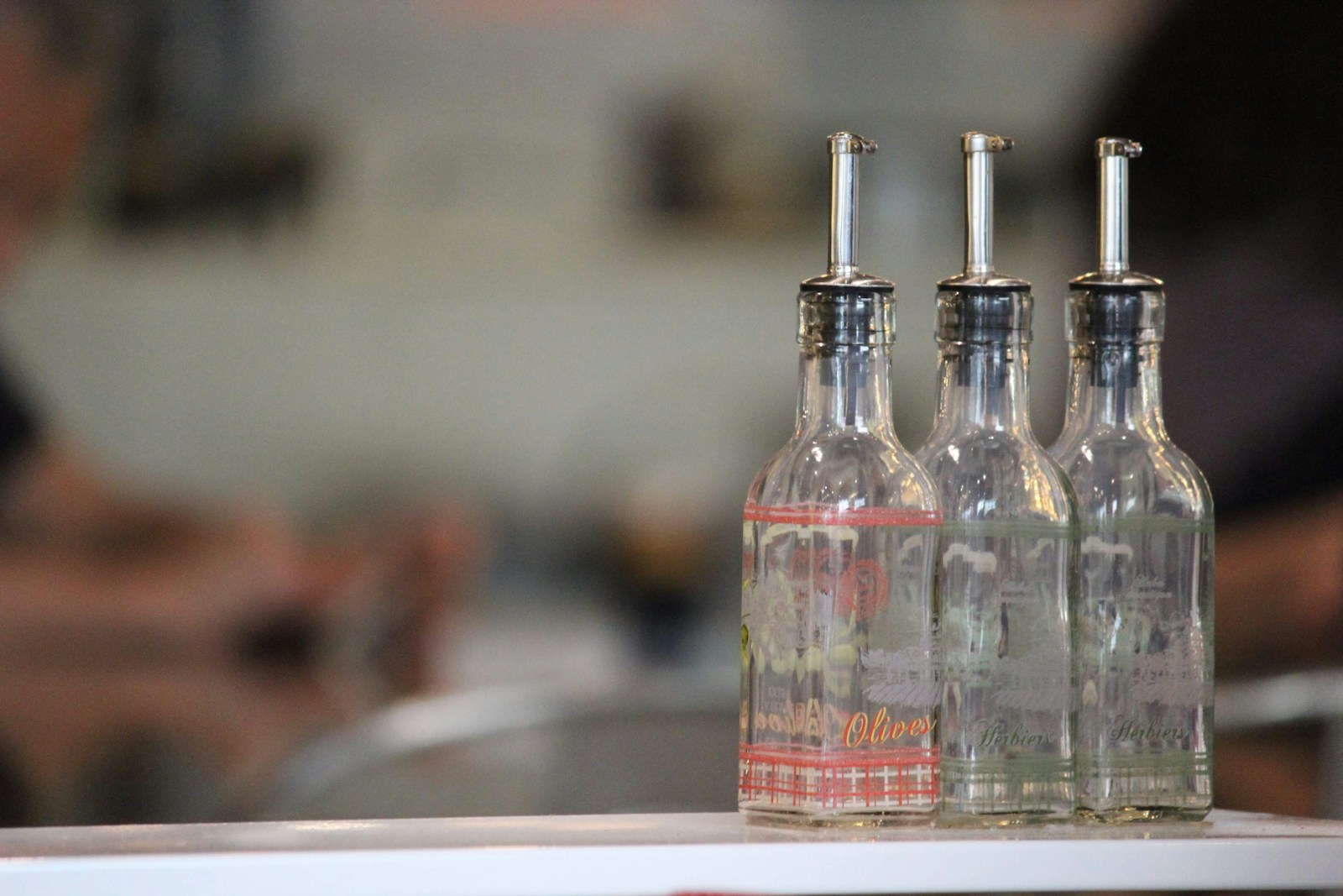 Three clear glass bottles with pour spouts on a white counter