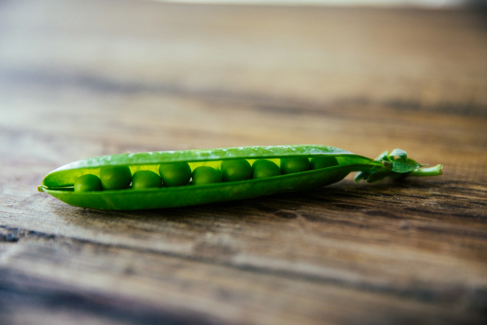A single split pea pod showing a row of plump green peas