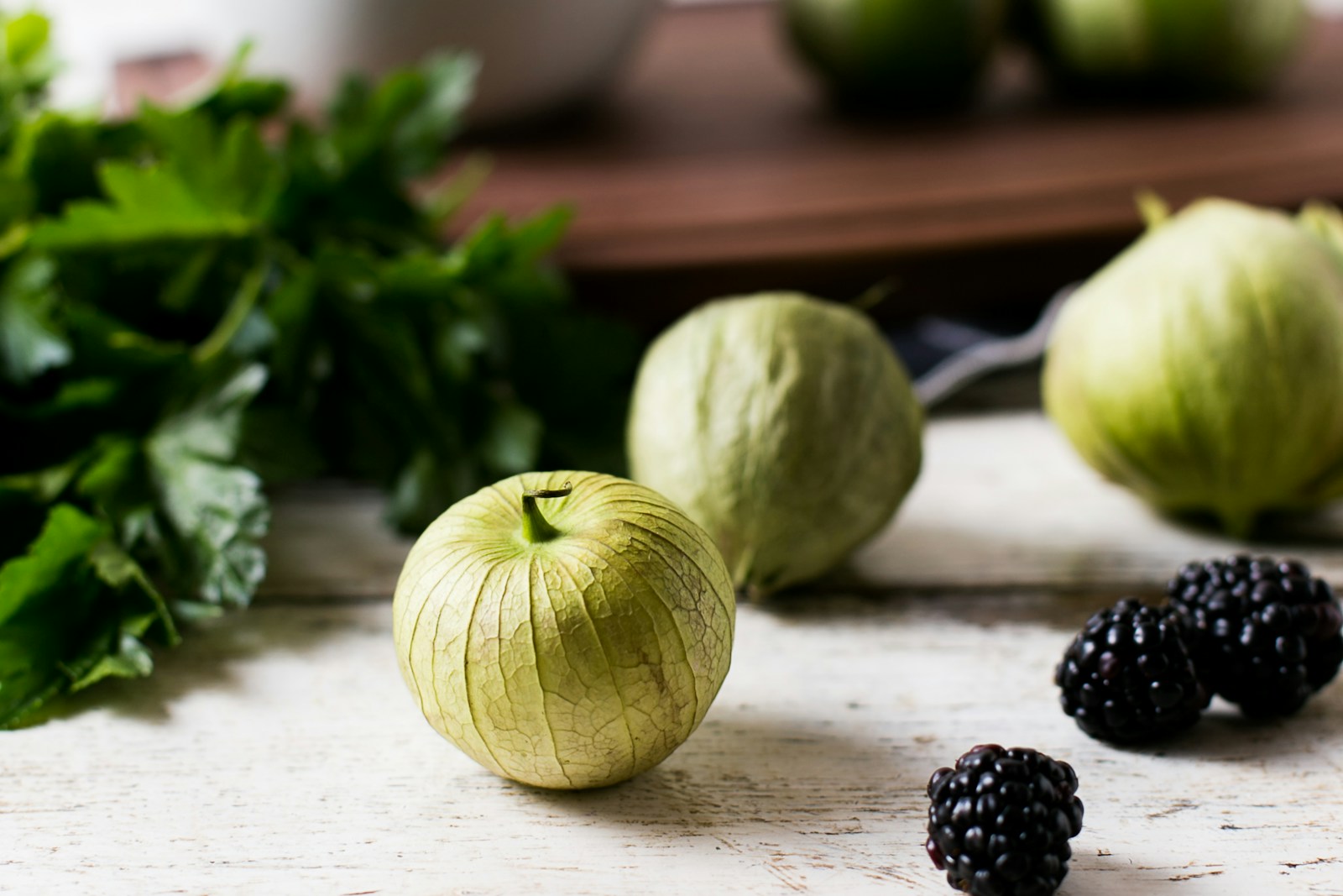 Husked tomatillos on a white table beside fresh herbs and blackberries