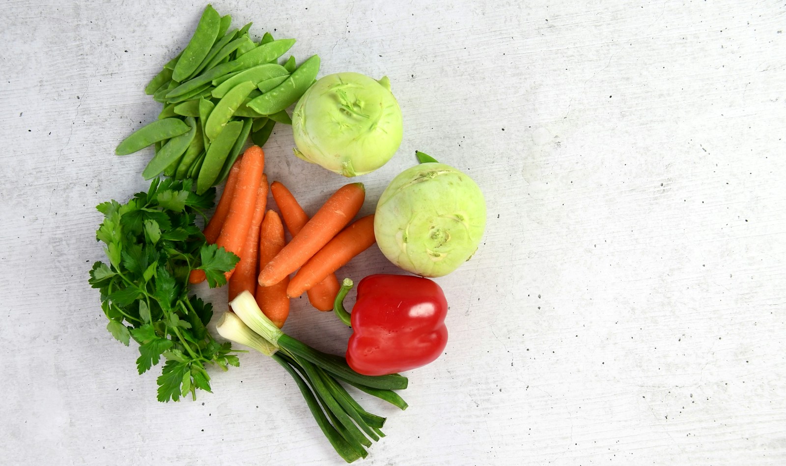 Two trimmed green kohlrabi bulbs beside carrots, snow peas, parsley and a red pepper